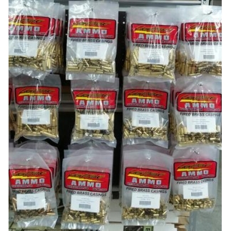 Store display with multiple plastic bags of fired brass casings labeled AMMO, arranged in rows on a shelf.