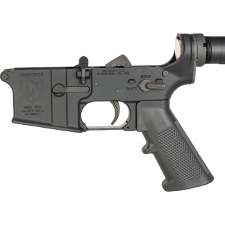Close-up of a black AR-style lower receiver with pistol grip and safety selector set to Safe, showing trigger and branding.